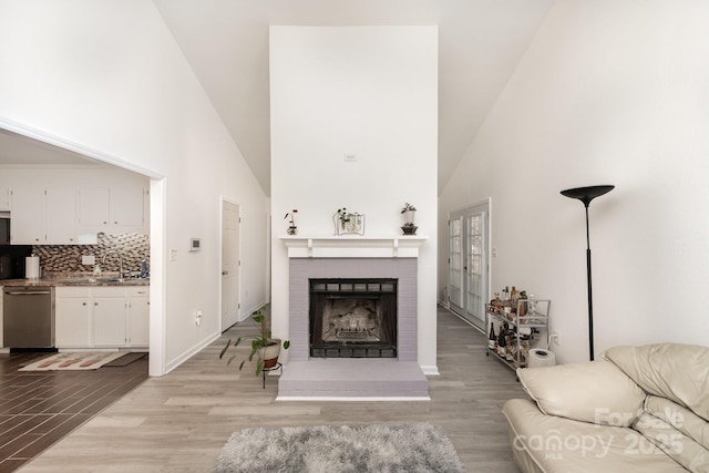 living room featuring a brick fireplace, light wood-style flooring, high vaulted ceiling, and baseboards