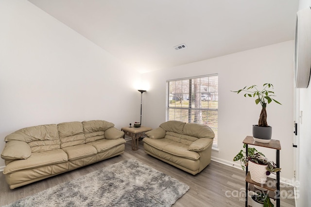 living room featuring light wood-style flooring, visible vents, vaulted ceiling, and baseboards