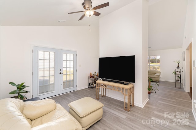 living room with high vaulted ceiling, light wood-style flooring, baseboards, and french doors