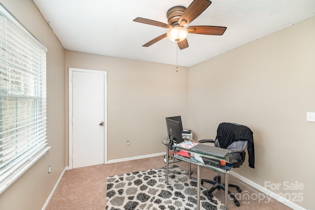 carpeted office space featuring a ceiling fan and baseboards