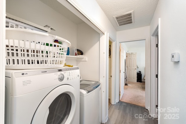 laundry room with laundry area, visible vents, wood finished floors, a textured ceiling, and washer and dryer