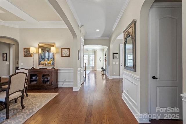 entryway featuring arched walkways, ornamental molding, wood finished floors, and a decorative wall