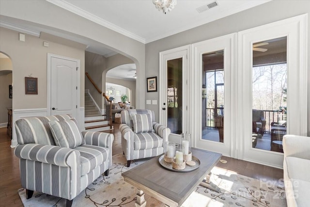 living area featuring arched walkways, wood finished floors, visible vents, stairway, and crown molding