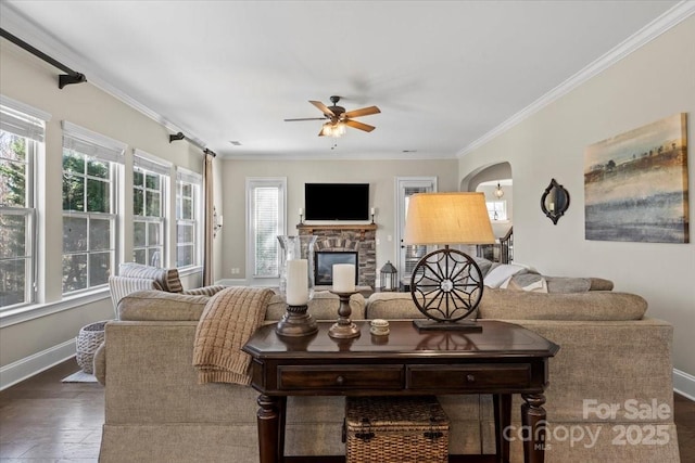 living area with arched walkways, crown molding, ceiling fan, wood finished floors, and baseboards