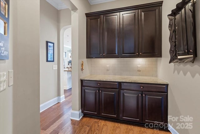 kitchen featuring arched walkways, decorative backsplash, light wood-style floors, dark brown cabinetry, and baseboards