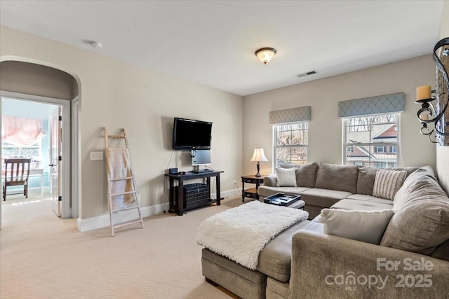 carpeted living room featuring arched walkways, visible vents, and baseboards