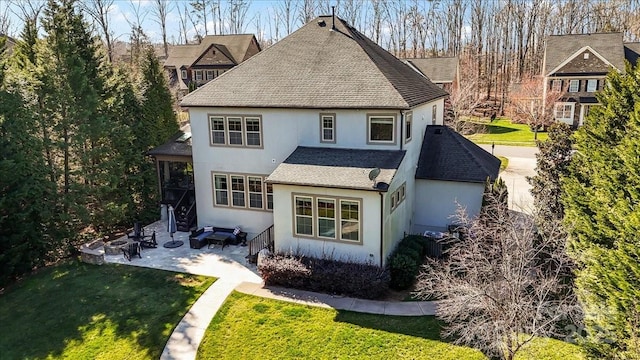 back of house featuring a shingled roof, a patio area, a lawn, and stucco siding