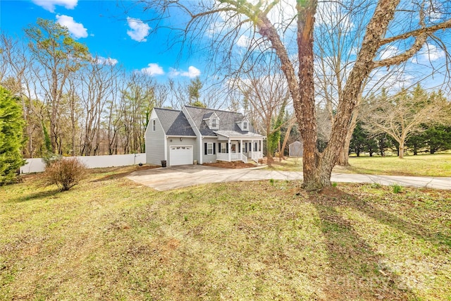 new england style home featuring a porch, fence, a garage, driveway, and a front lawn