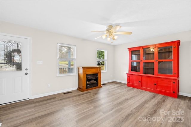 unfurnished living room featuring baseboards, visible vents, a ceiling fan, wood finished floors, and a fireplace