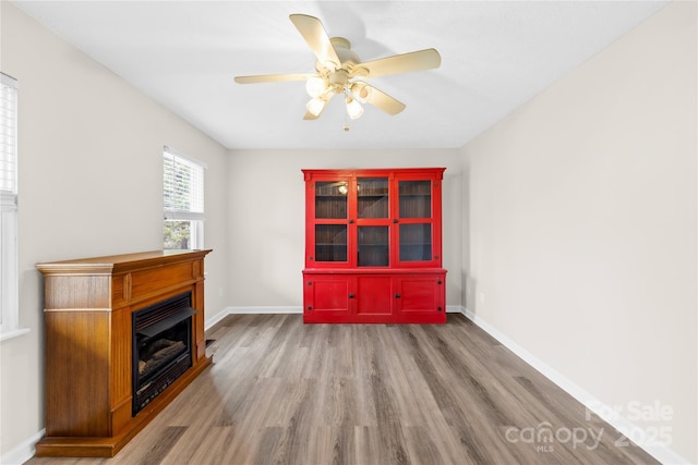 interior space with ceiling fan, a fireplace, wood finished floors, and baseboards