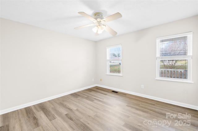 spare room with a ceiling fan, visible vents, baseboards, and wood finished floors