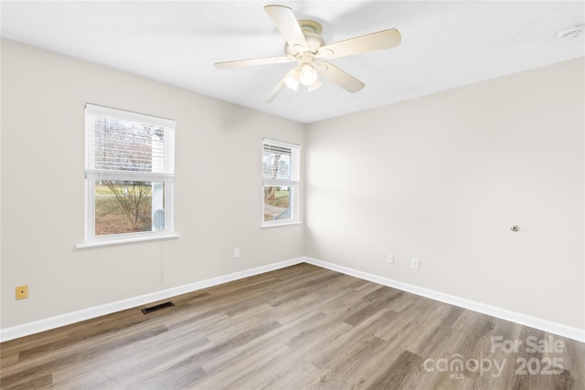 spare room with a ceiling fan, wood finished floors, visible vents, and baseboards