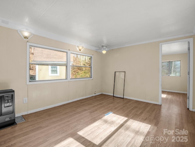 empty room with baseboards, ceiling fan, heating unit, and wood finished floors