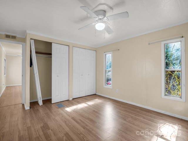 unfurnished bedroom with wood finished floors, visible vents, baseboards, multiple closets, and ornamental molding