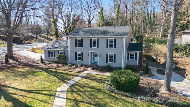 colonial house with driveway, a chimney, and a front lawn