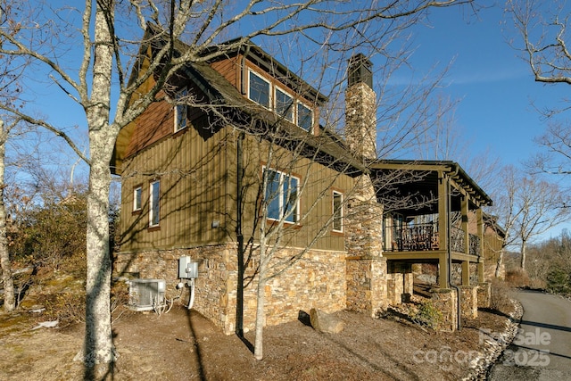 view of side of property with stone siding, central AC, a chimney, and a balcony