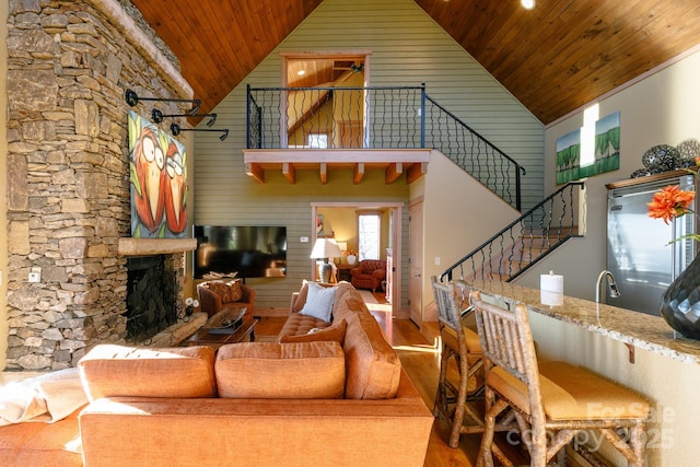 living area featuring a fireplace with raised hearth, high vaulted ceiling, wood finished floors, wood ceiling, and stairs