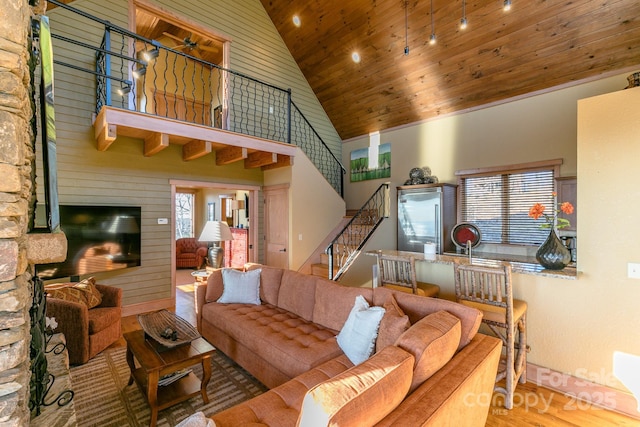 living room featuring wooden ceiling, wood finished floors, stairs, a fireplace, and high vaulted ceiling