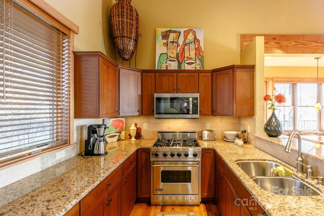 kitchen with stainless steel appliances, a sink, light wood-style floors, decorative backsplash, and light stone countertops