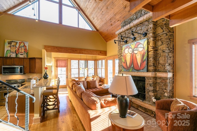 living room with light wood-style floors, a wealth of natural light, wood ceiling, and a stone fireplace