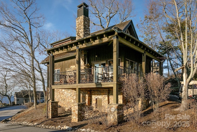 back of property featuring a balcony, stone siding, a chimney, and board and batten siding