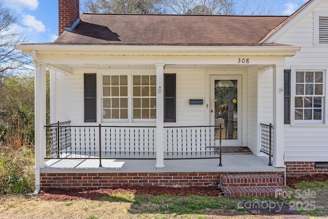 view of exterior entry with a porch, crawl space, a shingled roof, and a chimney