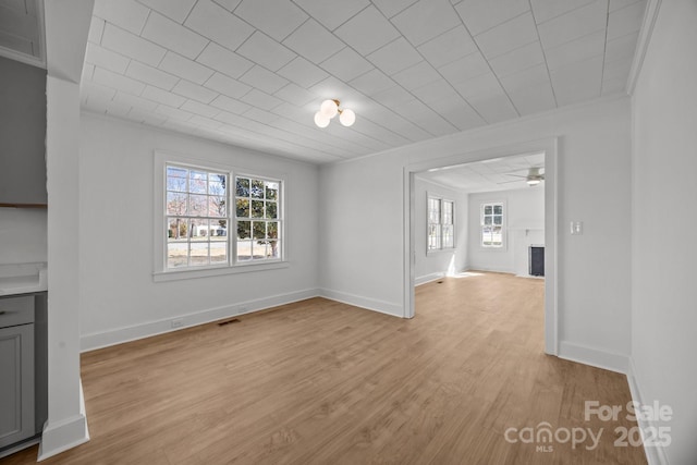 unfurnished living room featuring baseboards, visible vents, ornamental molding, light wood-style floors, and a fireplace