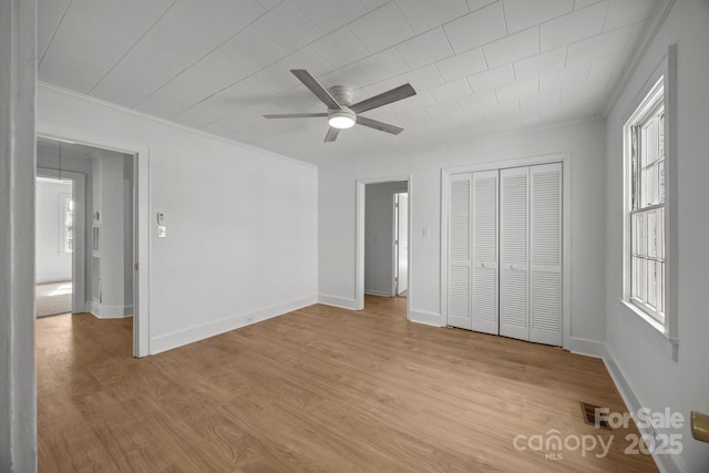 unfurnished bedroom with baseboards, ornamental molding, a closet, and light wood-style floors