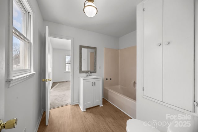 bathroom featuring toilet, a washtub, wood finished floors, vanity, and baseboards