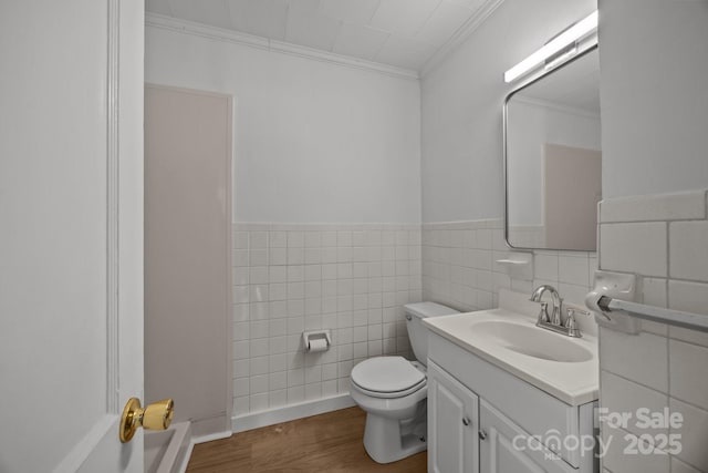 bathroom featuring toilet, wood finished floors, vanity, tile walls, and ornamental molding