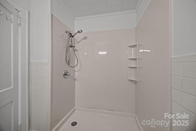 bathroom with a wainscoted wall, crown molding, tile walls, and walk in shower