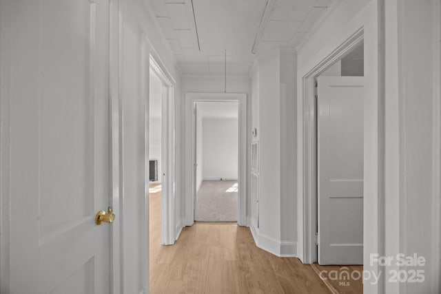 hallway featuring attic access, light wood-type flooring, and baseboards