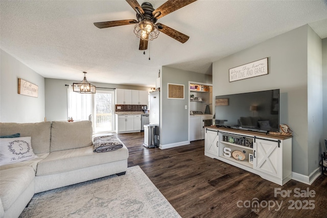 living area featuring baseboards, dark wood-type flooring, a textured ceiling, washer and dryer, and ceiling fan with notable chandelier