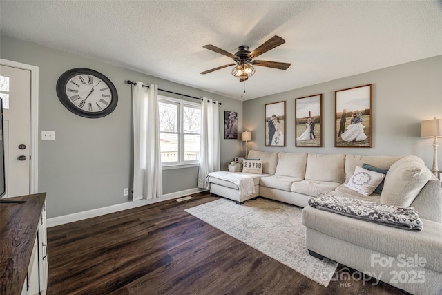 living area with dark wood-type flooring, ceiling fan, a textured ceiling, and baseboards