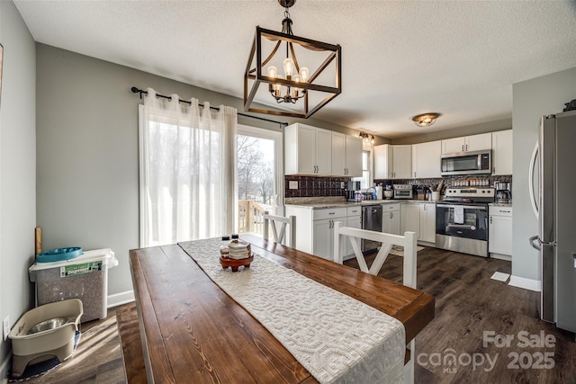 dining space with dark wood-style floors, a textured ceiling, a chandelier, and baseboards