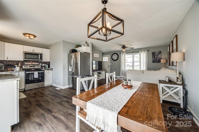 dining area with dark wood-style floors, ceiling fan with notable chandelier, and baseboards