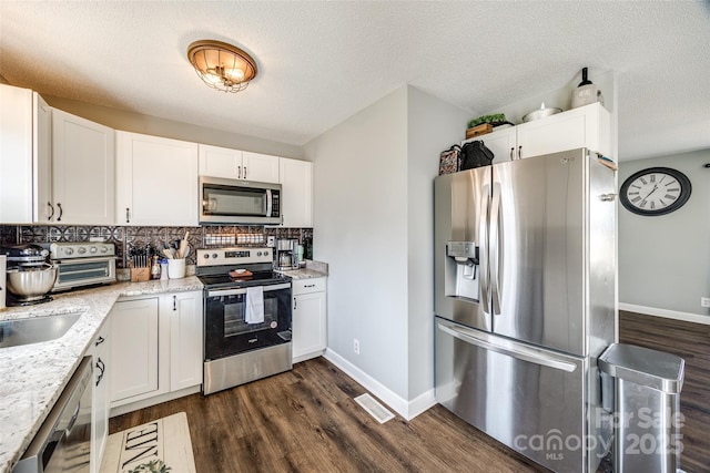 kitchen featuring light stone countertops, dark wood finished floors, stainless steel appliances, and decorative backsplash