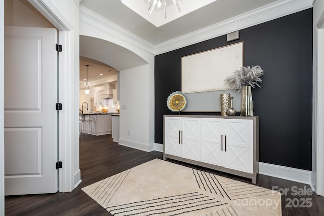 entrance foyer with baseboards, arched walkways, dark wood-type flooring, and ornamental molding