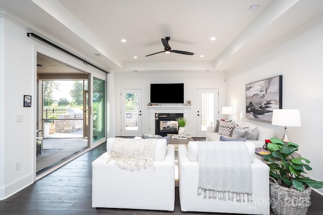 living area with a tray ceiling, dark wood-style flooring, recessed lighting, a multi sided fireplace, and baseboards