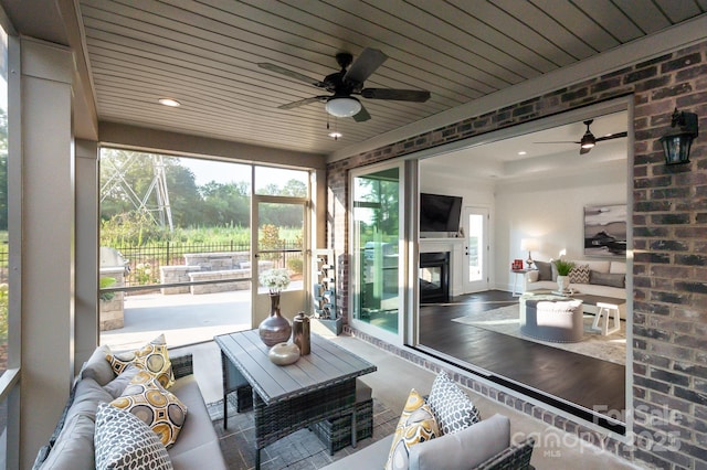 sunroom featuring a glass covered fireplace, wood ceiling, and a ceiling fan