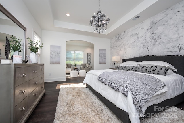 bedroom with arched walkways, an accent wall, visible vents, dark wood-style floors, and a tray ceiling