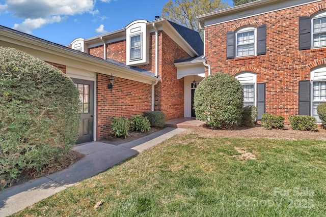 view of exterior entry with a lawn and brick siding