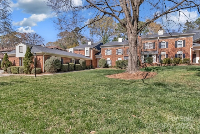georgian-style home with brick siding, a front yard, and a chimney