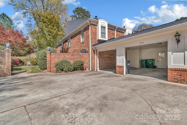 view of side of home featuring brick siding, a garage, concrete driveway, and roof with shingles
