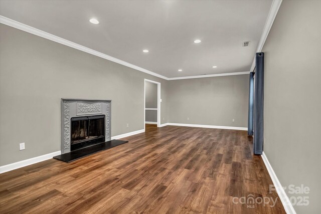 unfurnished living room featuring baseboards, ornamental molding, wood finished floors, and a fireplace with raised hearth