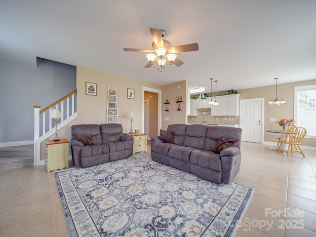 living room with light tile patterned floors, stairs, baseboards, and ceiling fan with notable chandelier