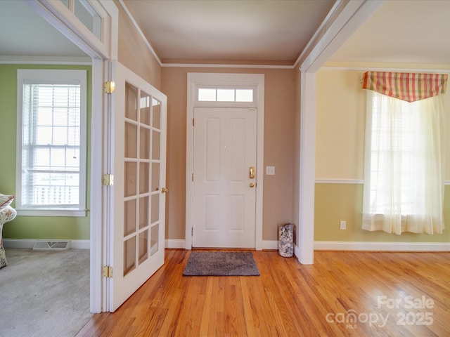 foyer entrance featuring ornamental molding, visible vents, baseboards, and wood finished floors