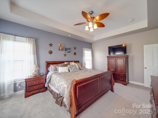 bedroom featuring light carpet, visible vents, baseboards, a raised ceiling, and a ceiling fan