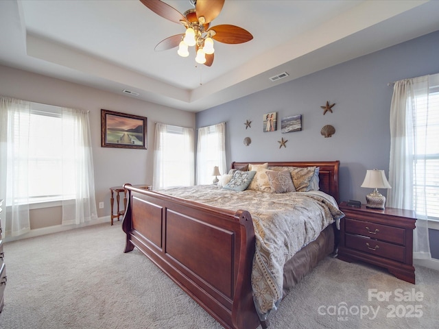 bedroom featuring visible vents, a tray ceiling, baseboards, and light colored carpet