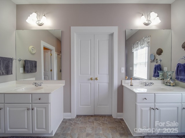 full bath featuring two vanities, a sink, and baseboards